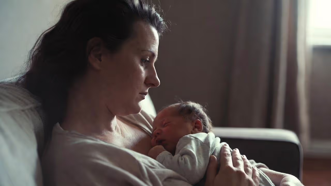 Woman holding a baby indoors while appearing emotionally distant
